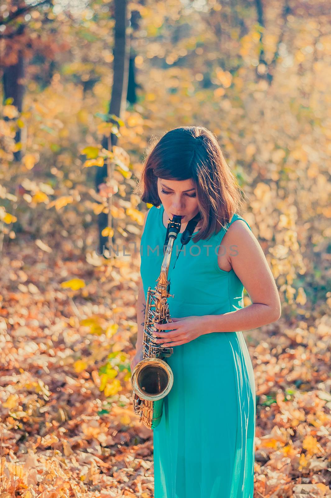 tender young girl with dark hair in a beautiful long blue dress plays the alto saxophone in a yellow autumn park by chernobrovin
