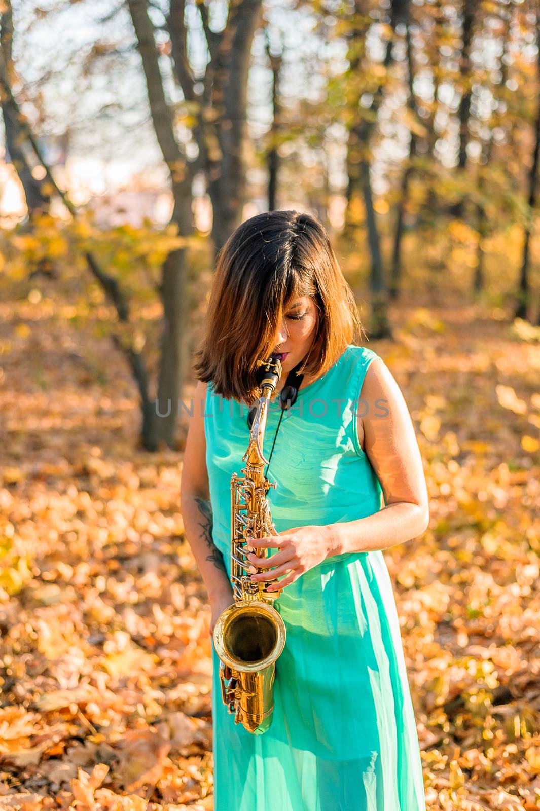 very beautiful young brunette girl in a luxurious long blue dress plays solo on her saxophone in the autumn forest