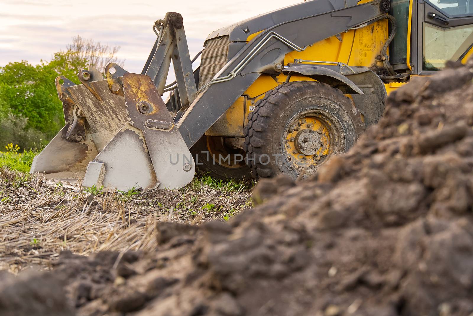 Yellow Excavator. yellow tractor on the field. Construction Machinery On Field. large yellow wheel loader aligns a piece of land for a new building. Tractor On Farmland
