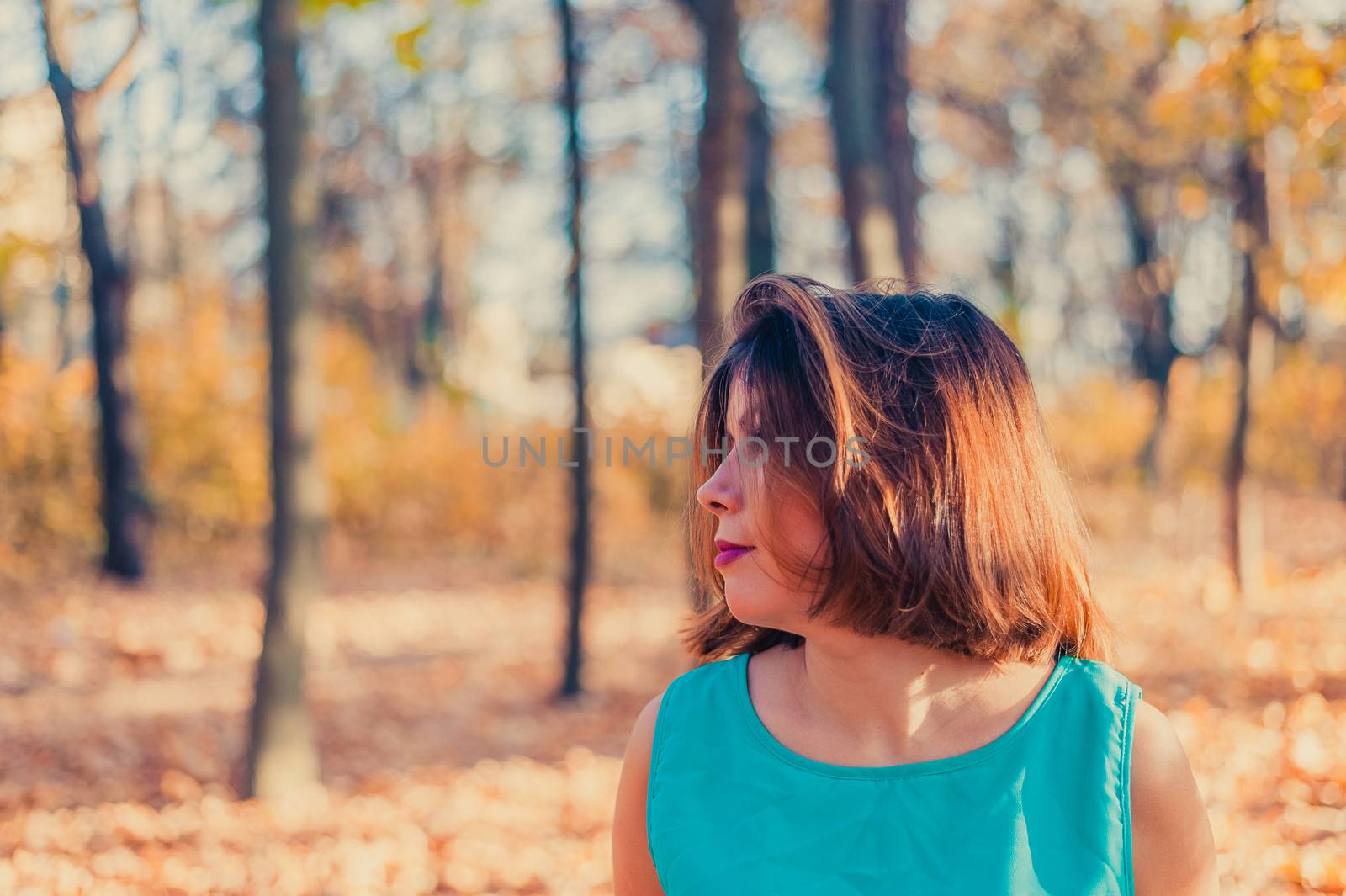 close side portrait of a young girl with black hair who looks away, standing in a golden autumn forest