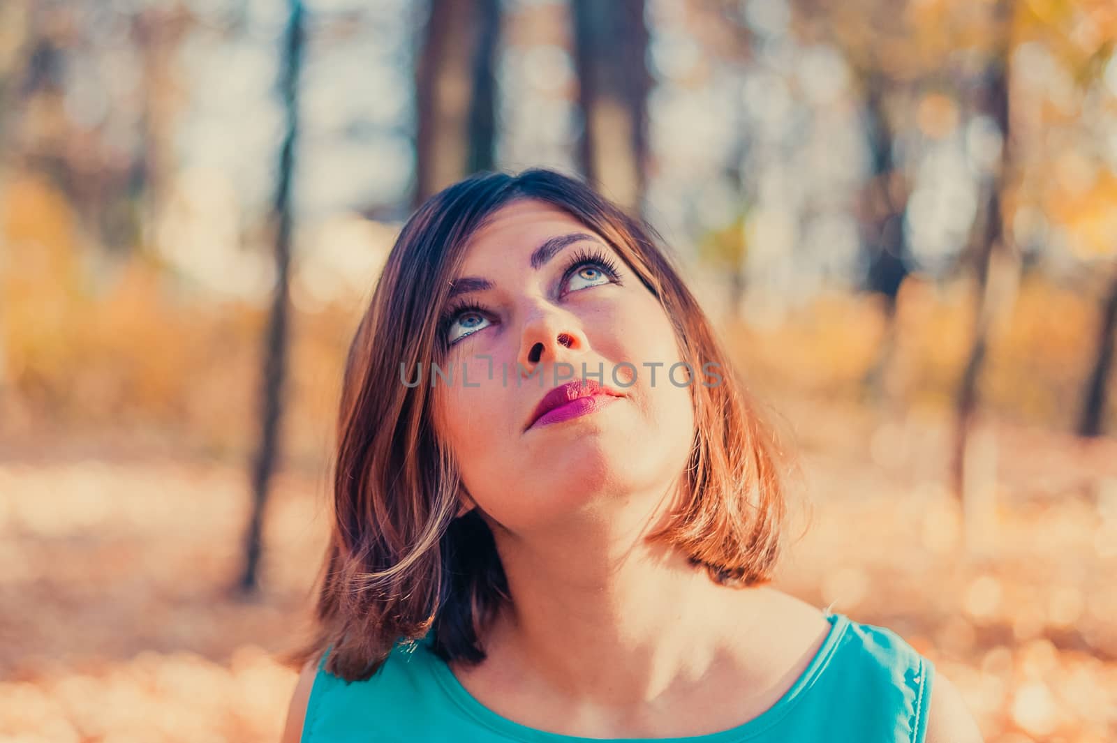 pretty red-haired teen girl in blue clothes looks up in the autumn park by chernobrovin