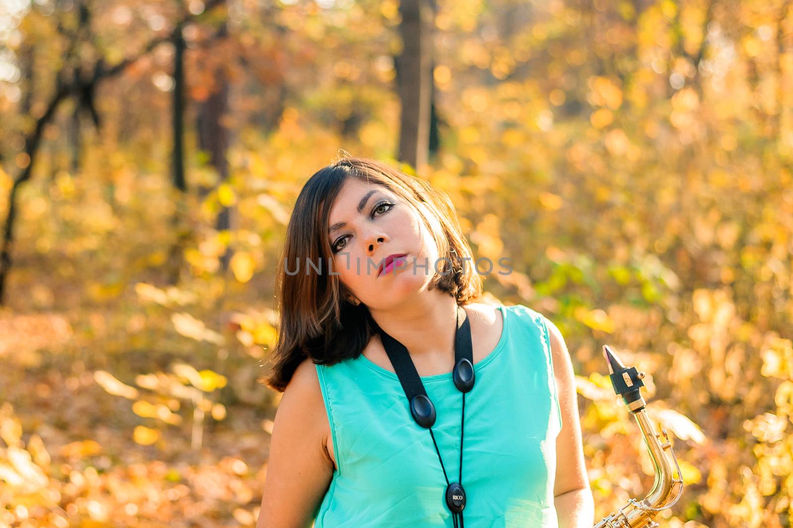 young beautiful black-haired saxophonist girl posing on a background of yellow leaves of an autumn park by chernobrovin