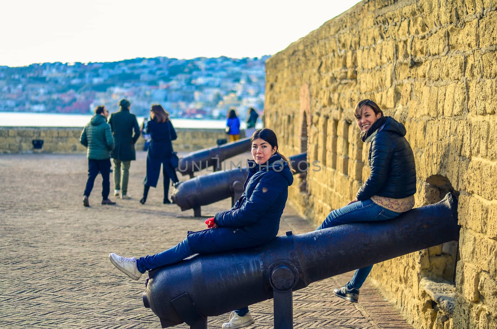 two women sit on the old guns and fortifications in the Castel dell'Ovo (Egg Castle) in Naples, Italy