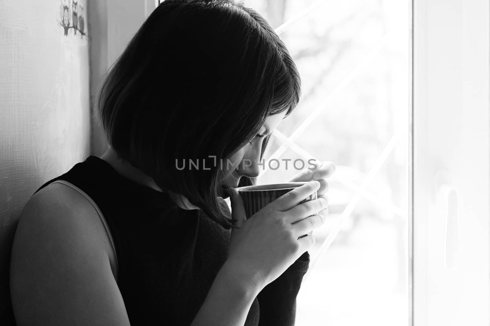 black and white portrait of a young brunette girl in black with a big cup of tea by the window