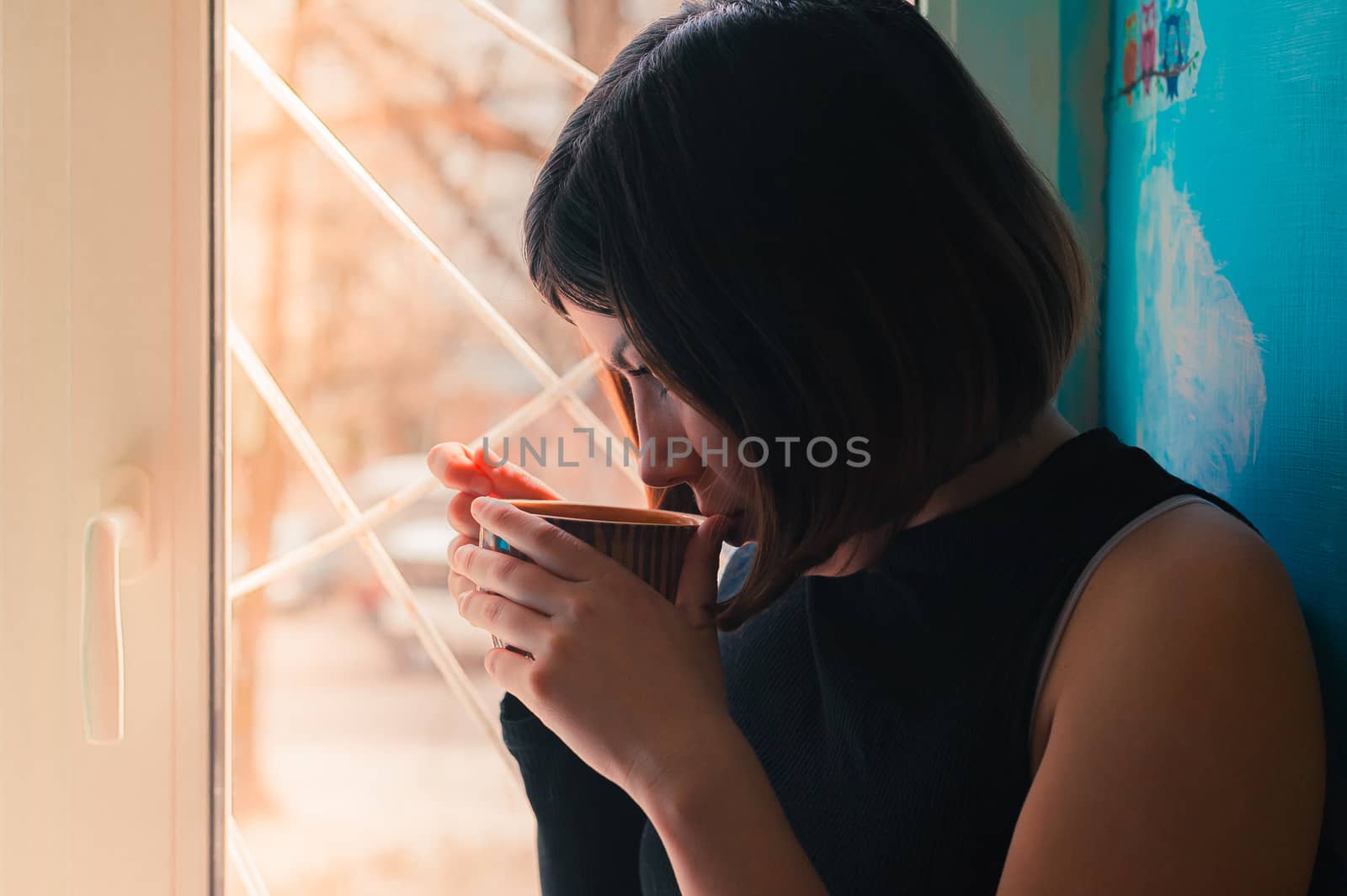 portrait of a young brunette girl in black with a big cup of tea by the window