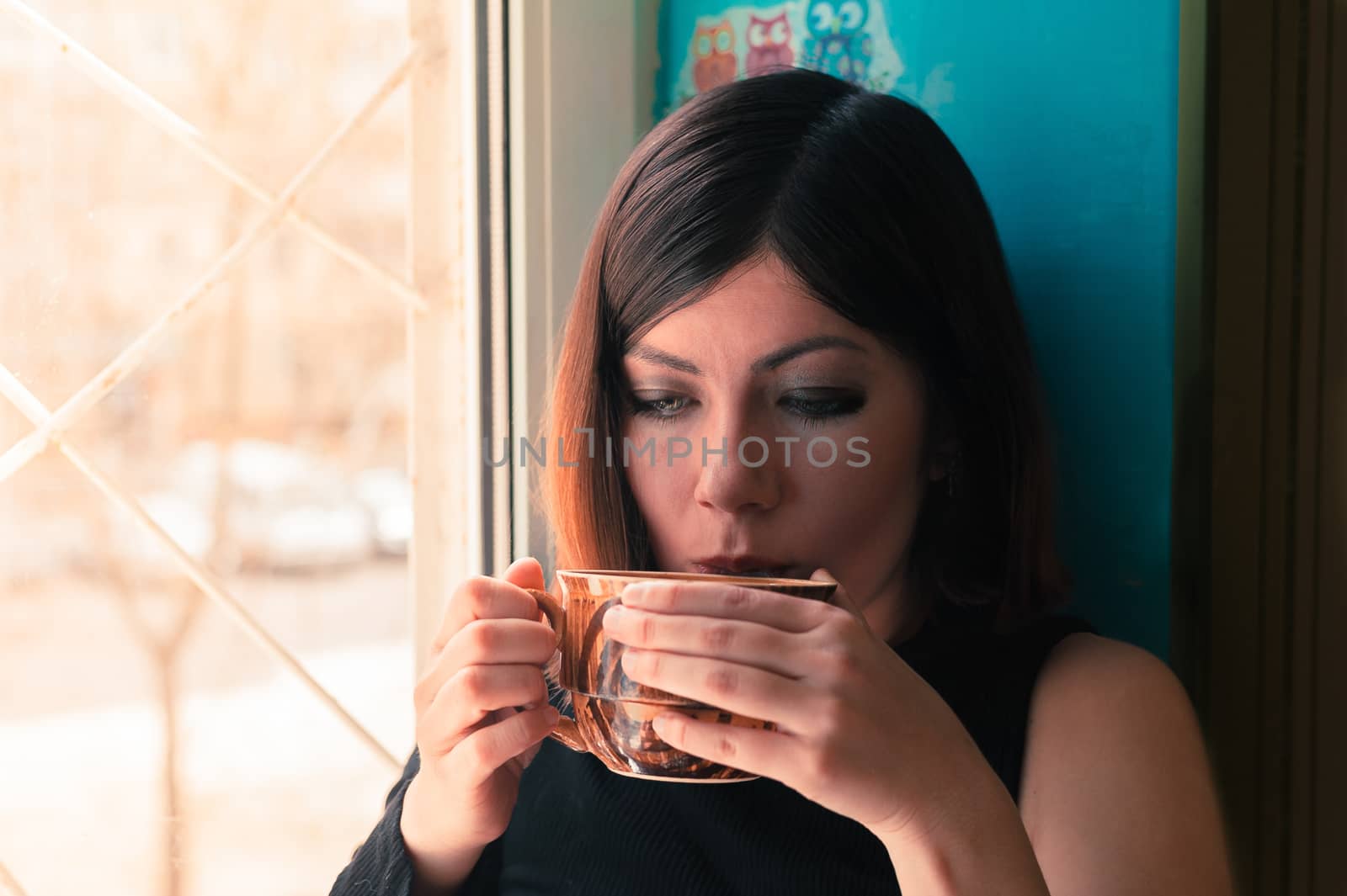 young woman with dark hair in black clothes is drinking tea from