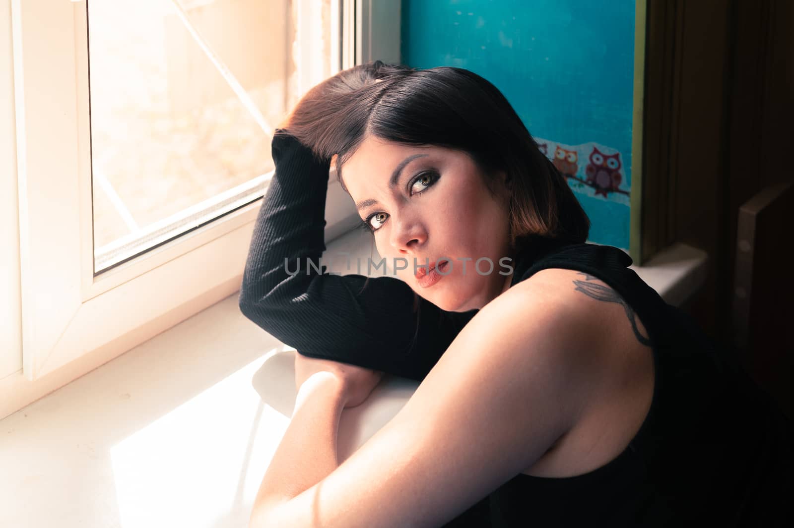 beautiful brunette girl in black clothes leaned on the windowsill near the window