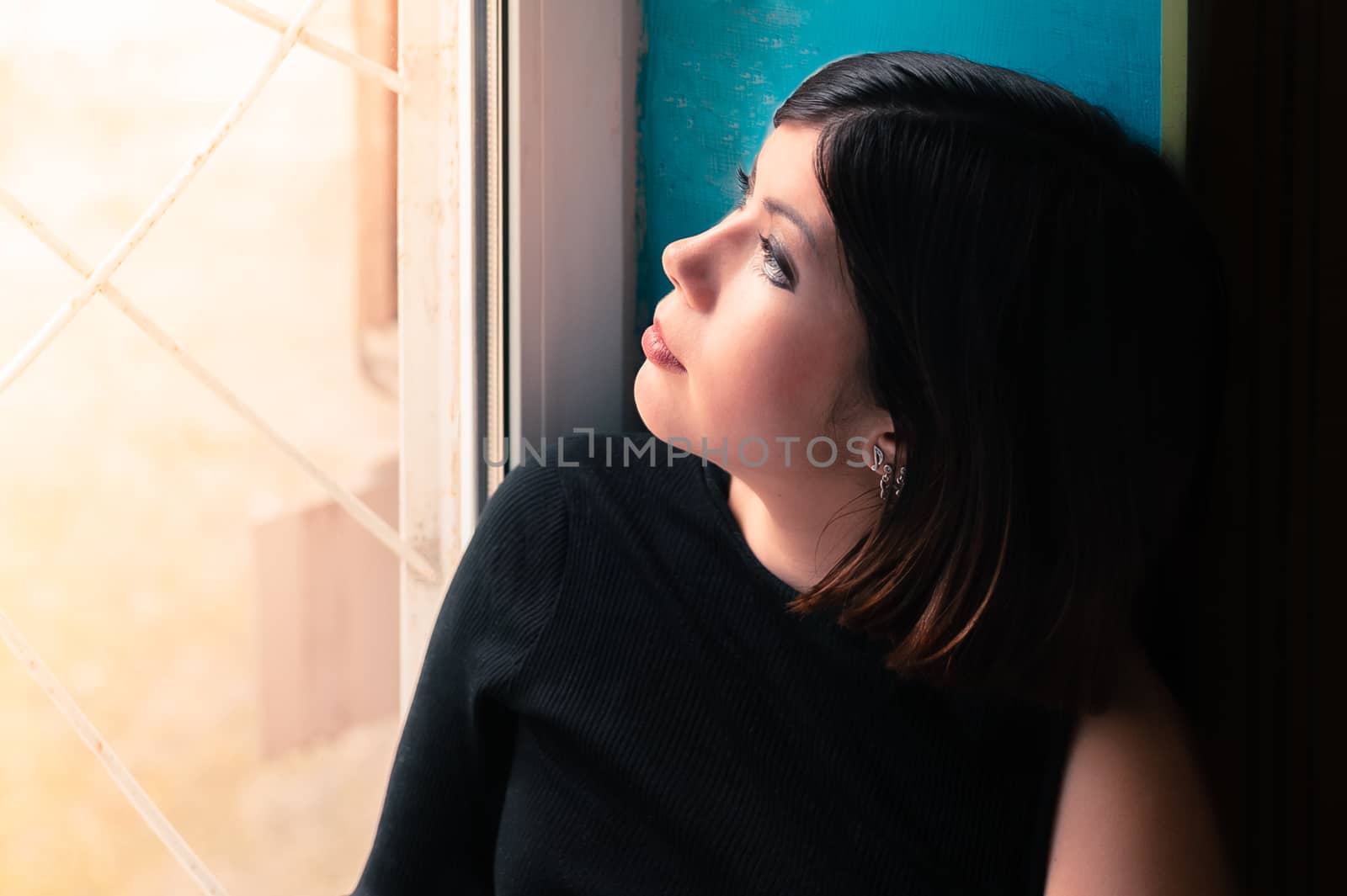 divine young girl with dark hair in black clothes looks out the window