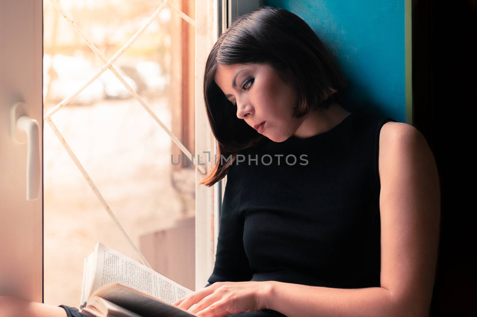 gorgeous young brunette woman in black clothes is reading a book
