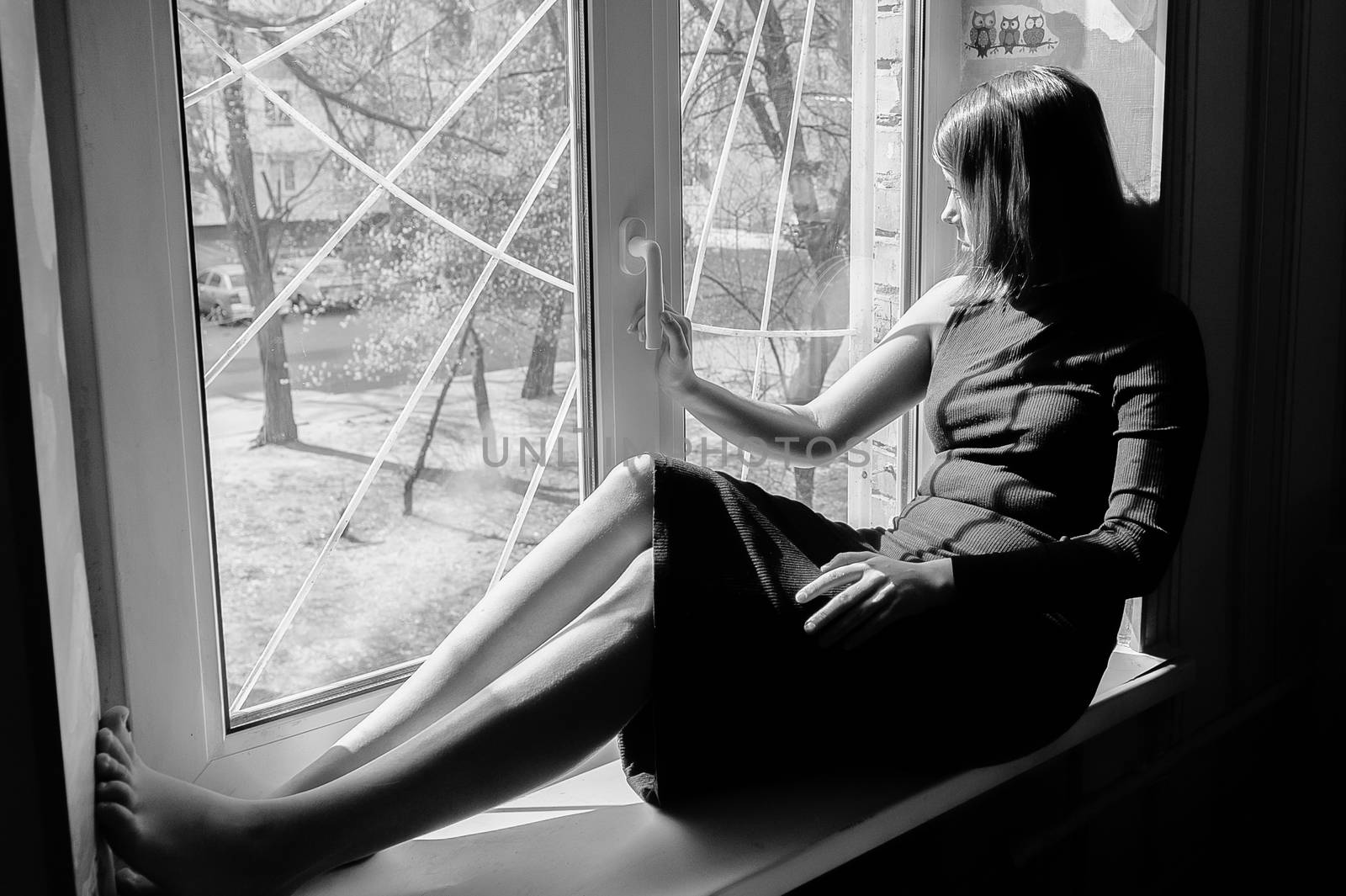 black and white portrait of a beautiful black-haired girl sitting on a windowsill in a long tight-fitting dark dress
