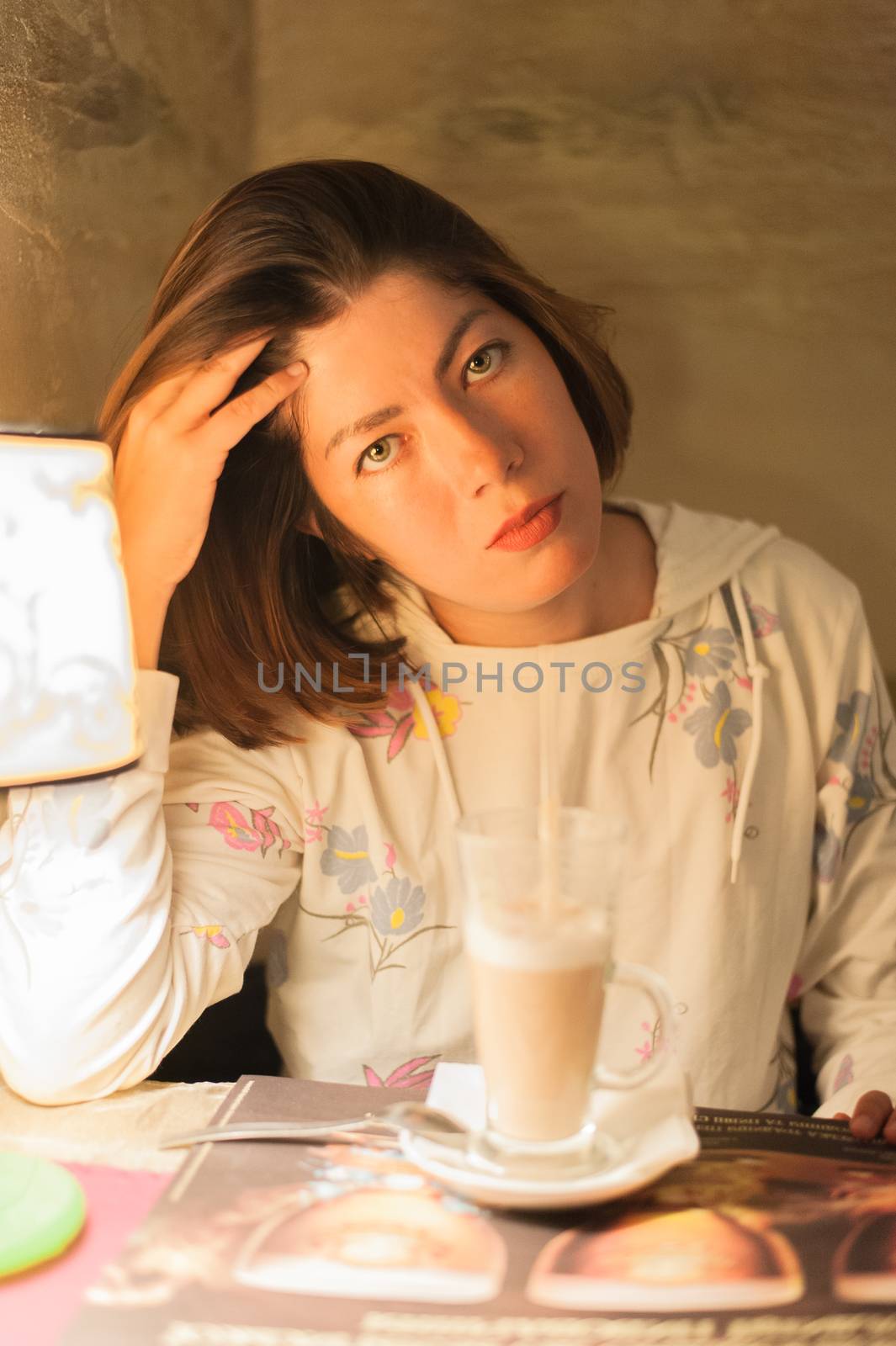 nice young brunette girl sitting at a table near a glass of latte macchiato