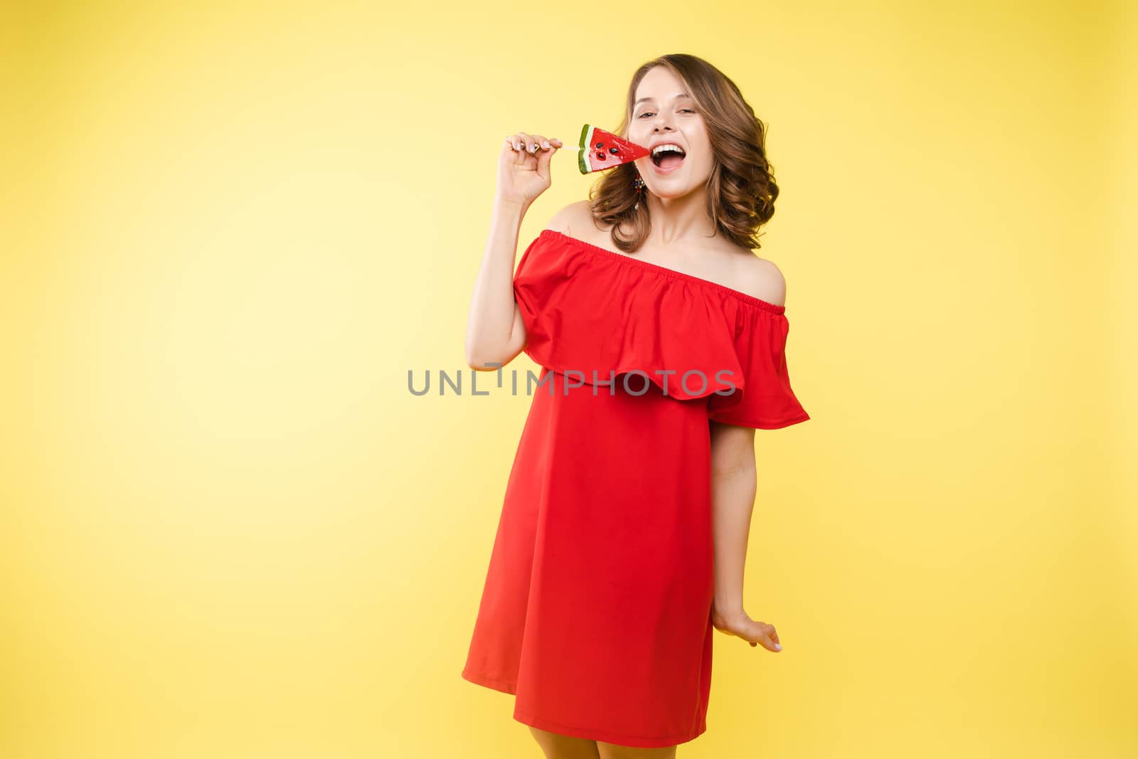 Close up portrait of attractive lovely girl in light dress handing lolipop isolated on yellow background