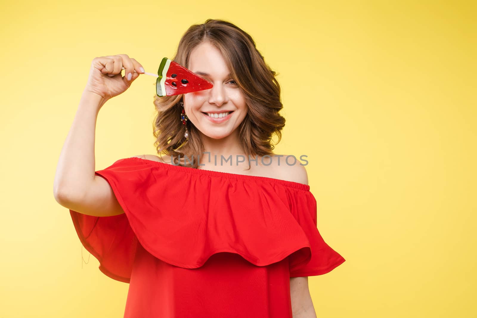 Close up portrait of attractive lovely girl in light dress handing lolipop isolated on yellow background