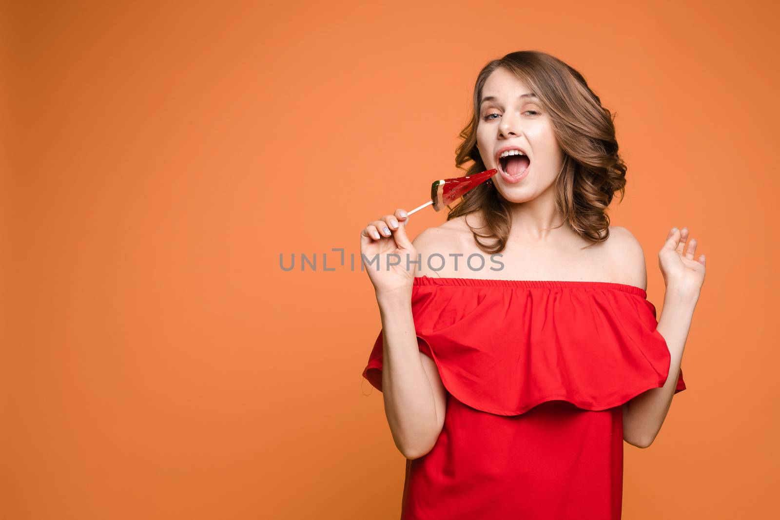 Close up portrait of attractive lovely girl in light dress handing lolipop isolated on yellow background