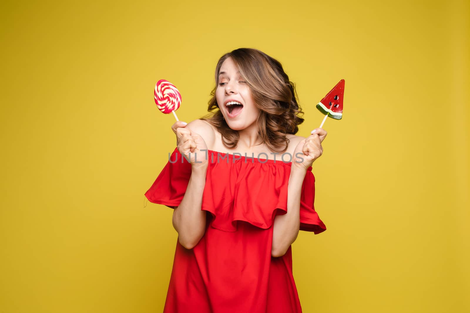 Close up portrait of attractive lovely girl in light dress handing lolipop isolated on yellow background