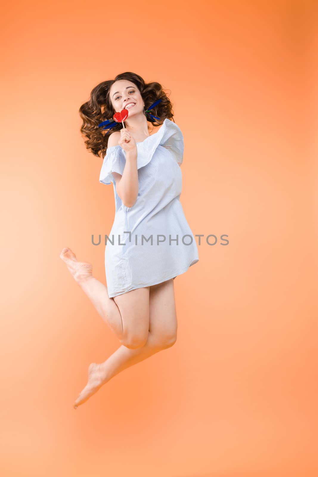 Close up portrait of attractive lovely girl in light dress handing lolipop isolated on yellow background