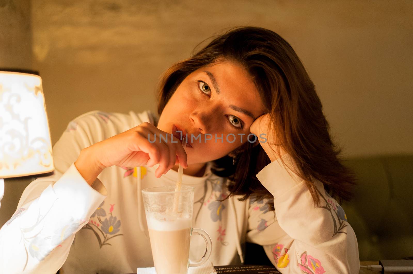 pretty young black-haired woman looking directly at the camera and drinking latte coffee