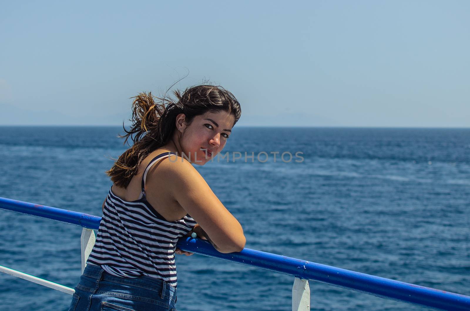 beautiful young girl with dark hair in a striped t-shirt and jeans stands on the deck of a ship at sea