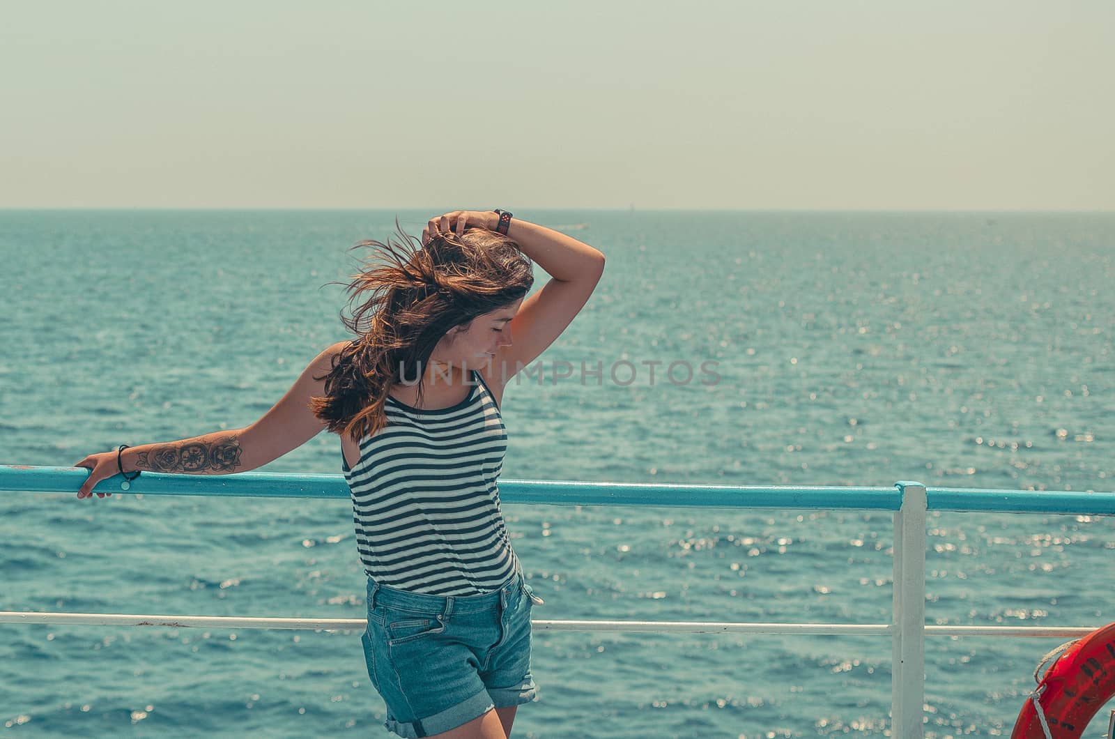 lovely young black-haired girl in a striped T-shirt and blue shorts posing on the deck of a ship on the high seas