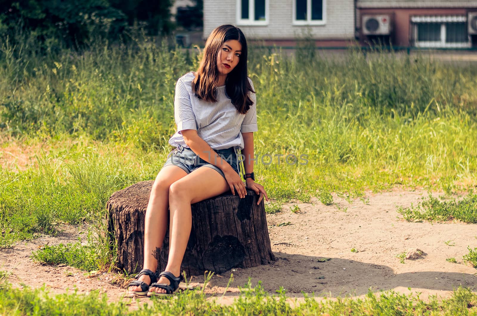 Teen Girl in a blue jeans shorts sitting on a Stump