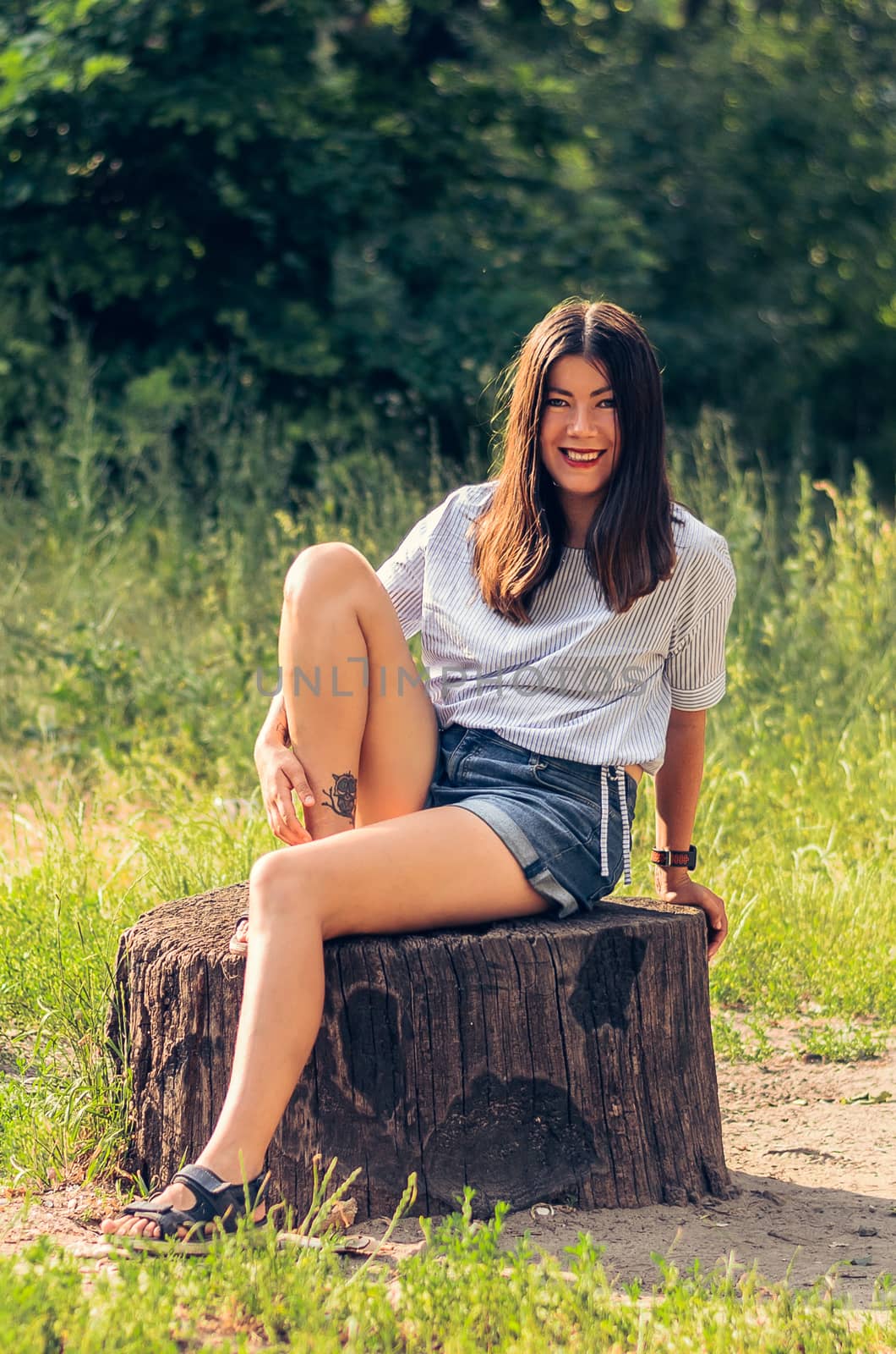Young beautiful brunette smiling girl posing on a stump. by chernobrovin