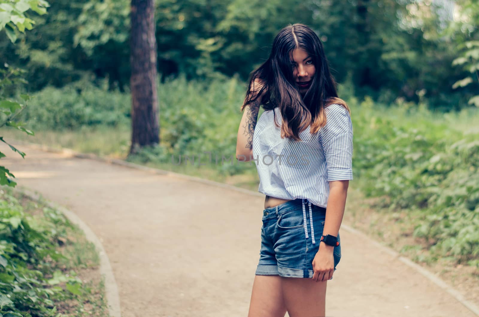 Young fashion woman with long dark hair posing on the road in a park.