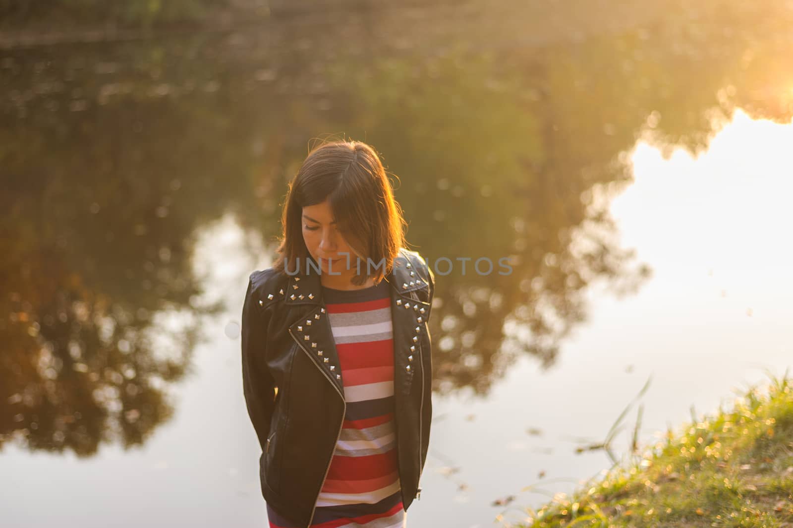 pretty teenager girl with black hair posing on a background of a forest lake in the sunshine by chernobrovin