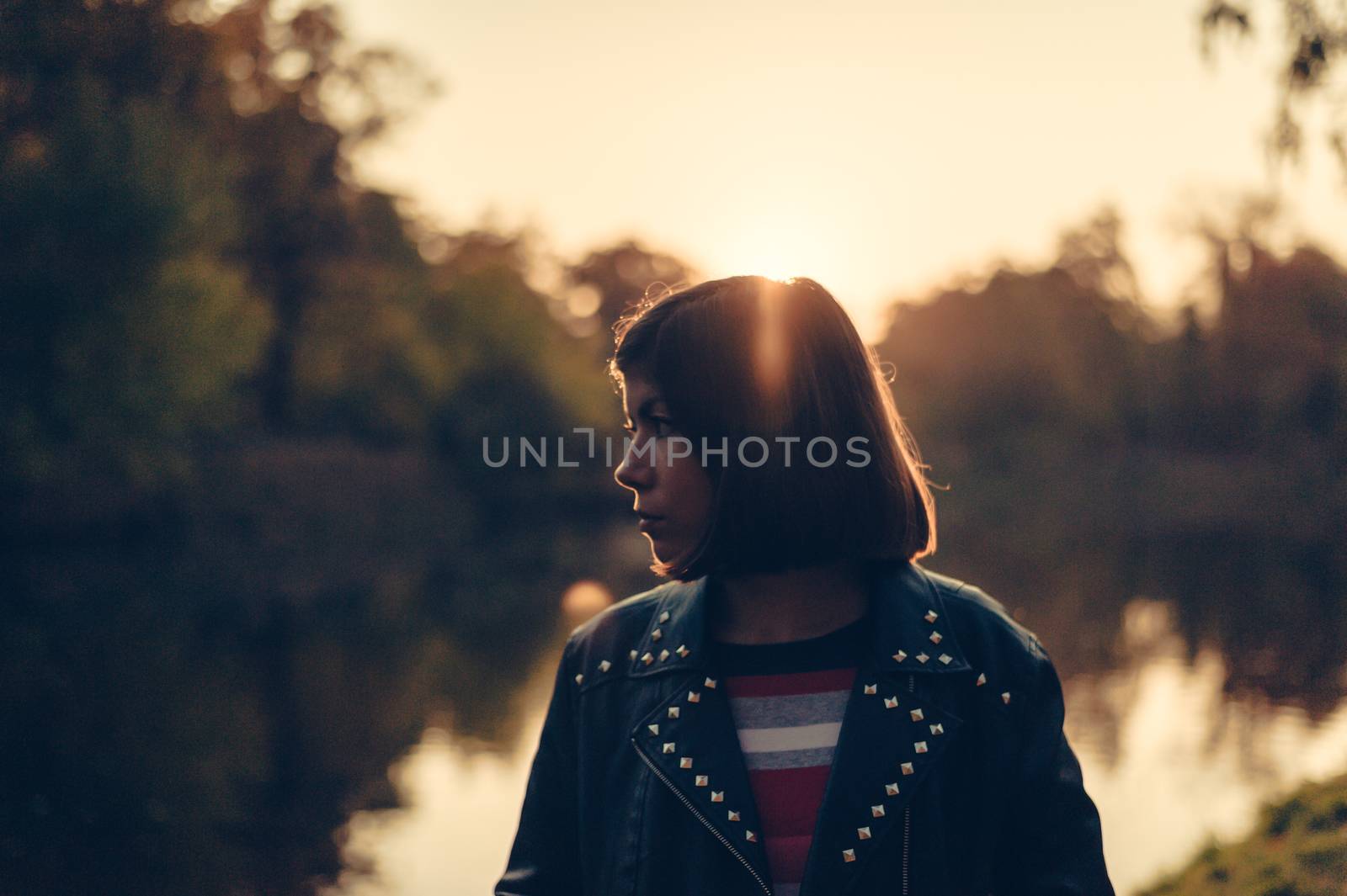 young girl in profile at dusk near a lake in a park by chernobrovin