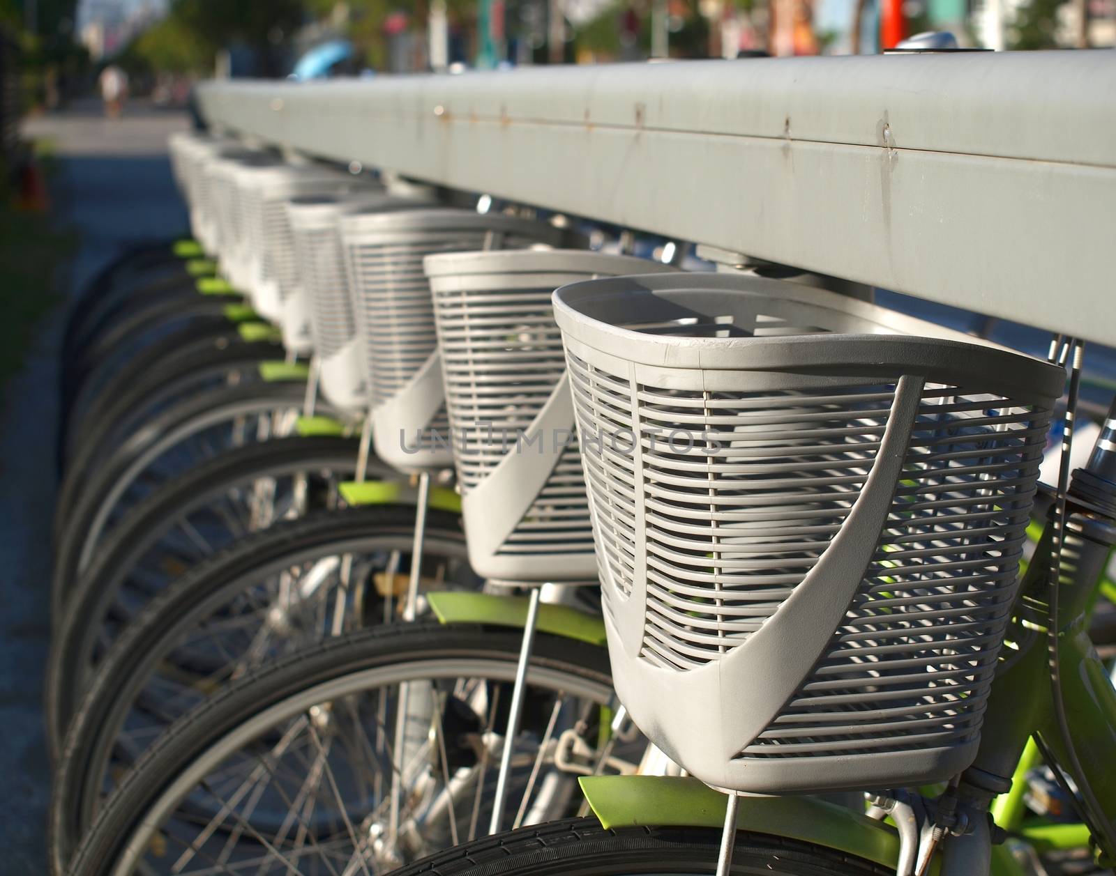 A row of green rental bicycles with gray baskets