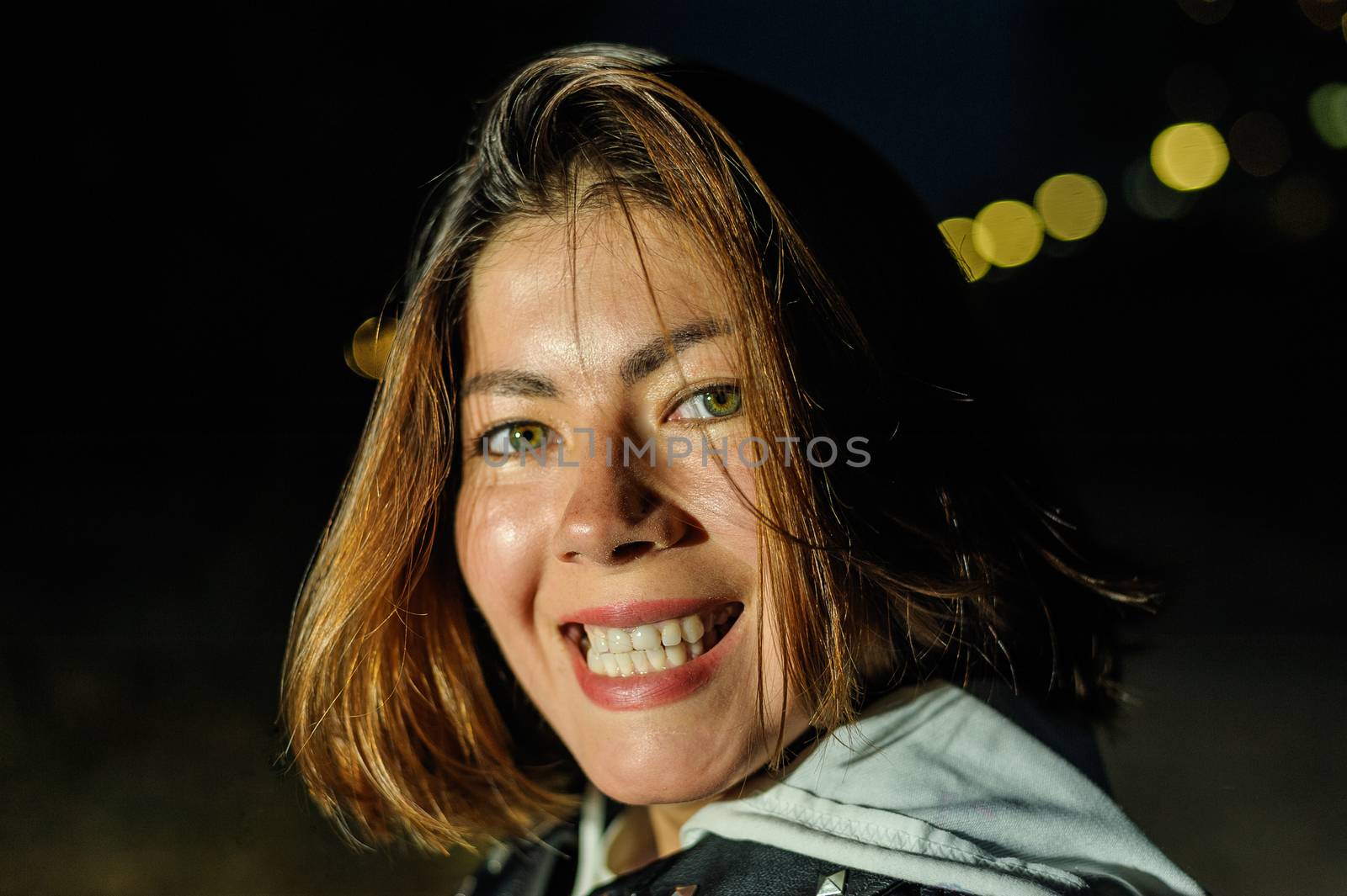 face of a beautiful smiling girl with dark hair on the background of the lights of the night city by chernobrovin