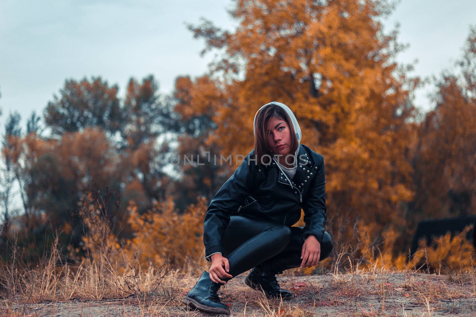 girl in black clothes squatted against a background of yellow autumn trees