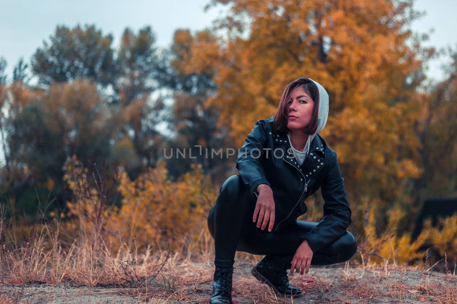 teenager girl in black leather clothes crouched on a background of yellow autumn forest