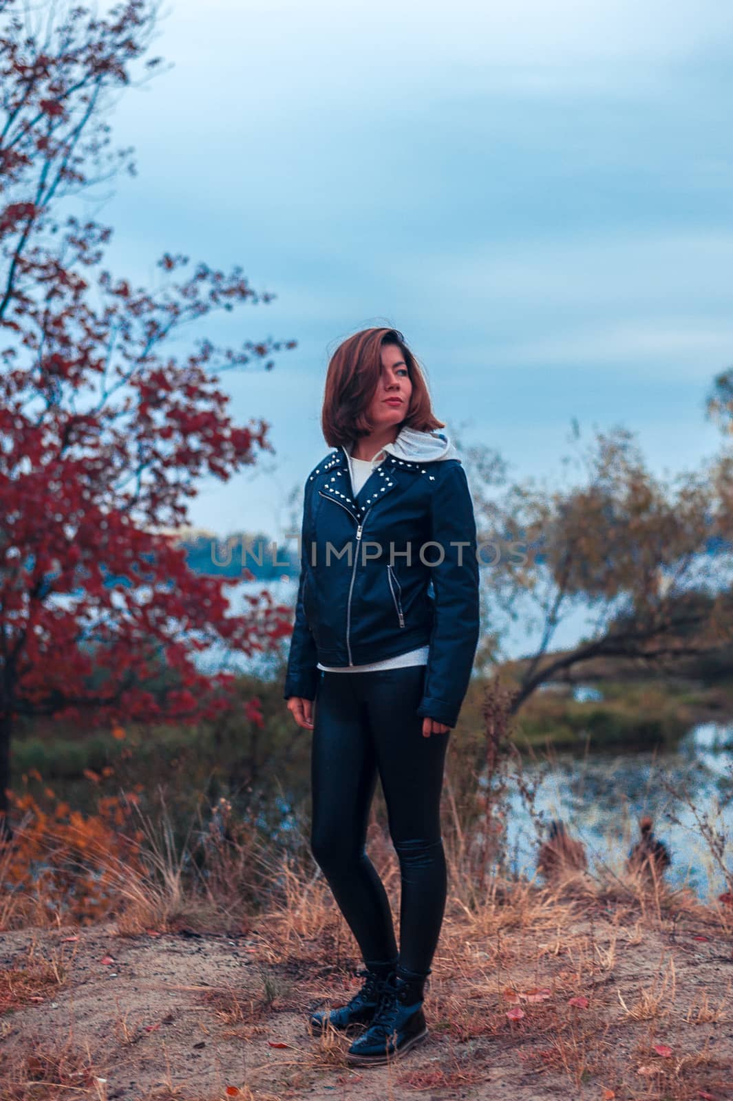 young dark-haired girl in black stands in the autumn forest near the lake