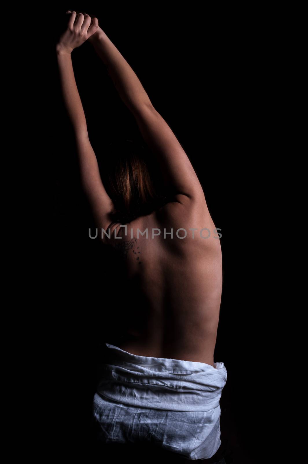 young pretty brunette woman stands with naked back in the dark with arms raised up