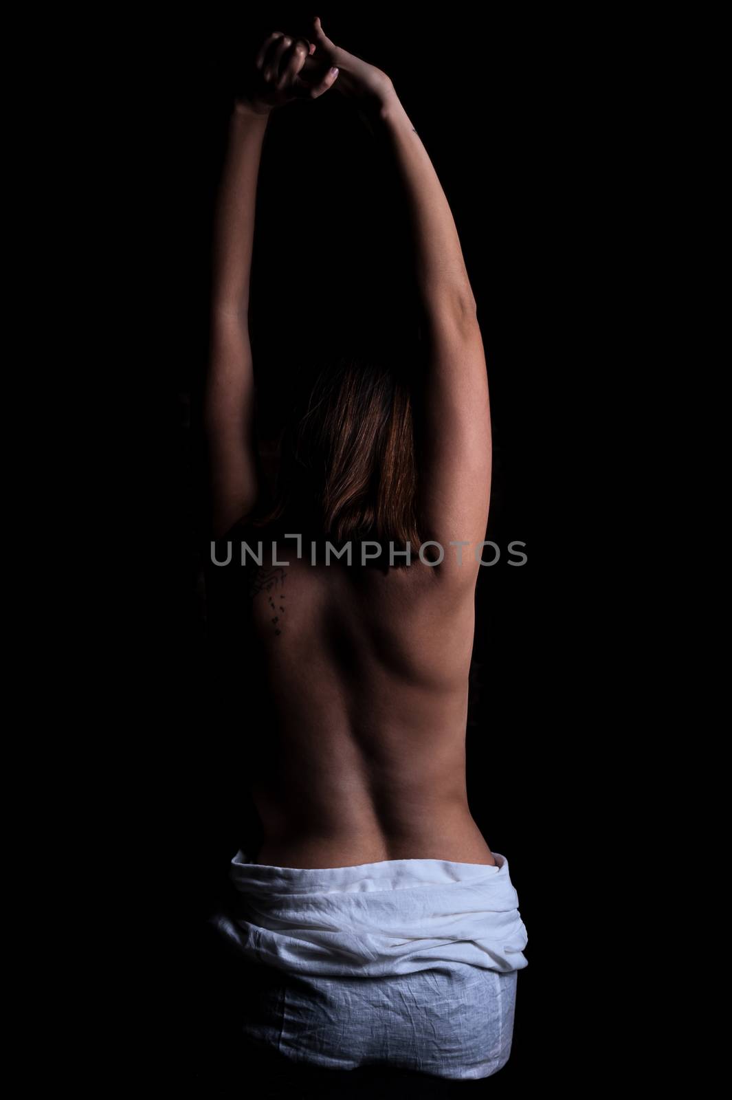 young thin brunette girl stands in the dark with a naked back with arms extended up