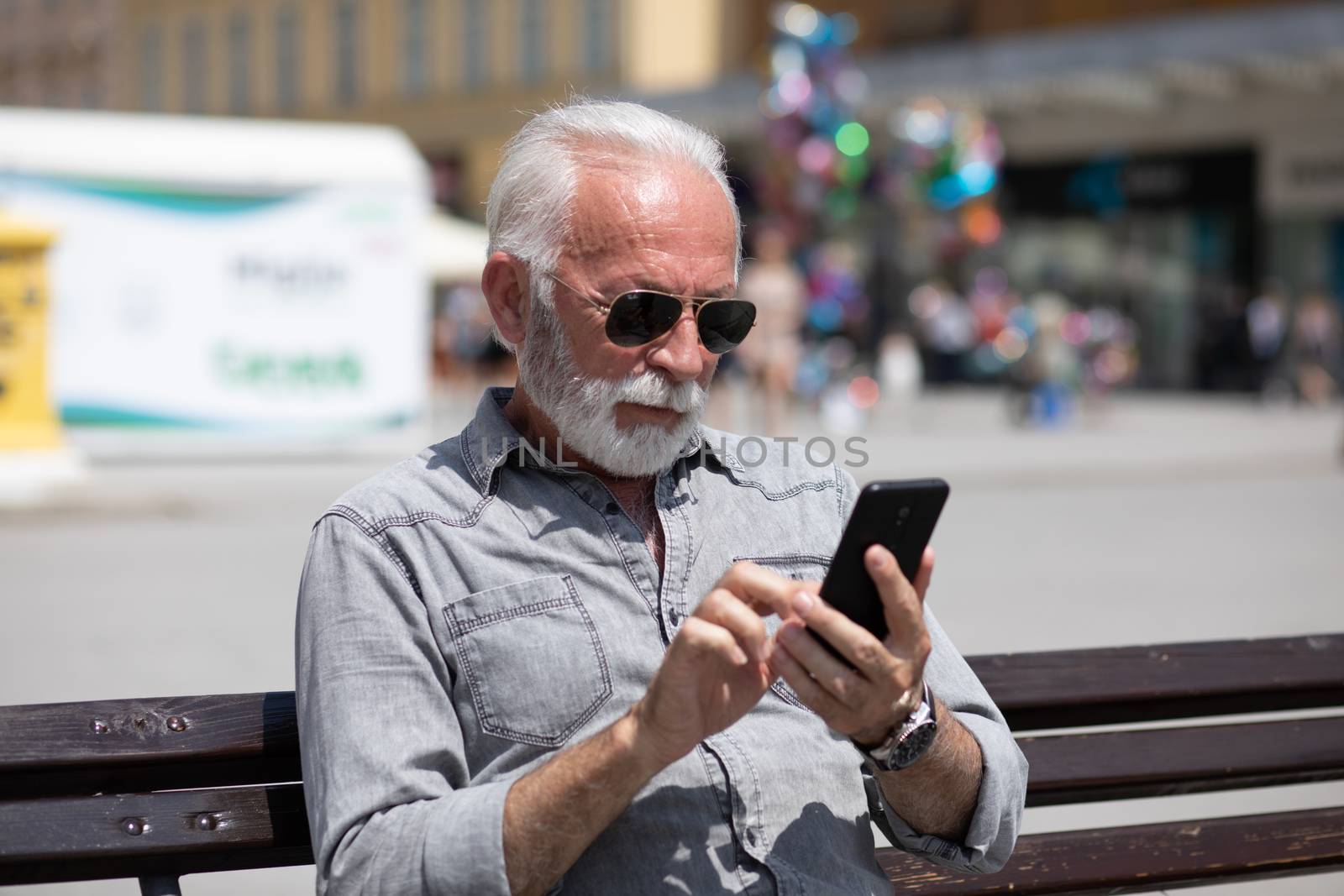 Old man use internet application on smartphone, urban city background stock photo