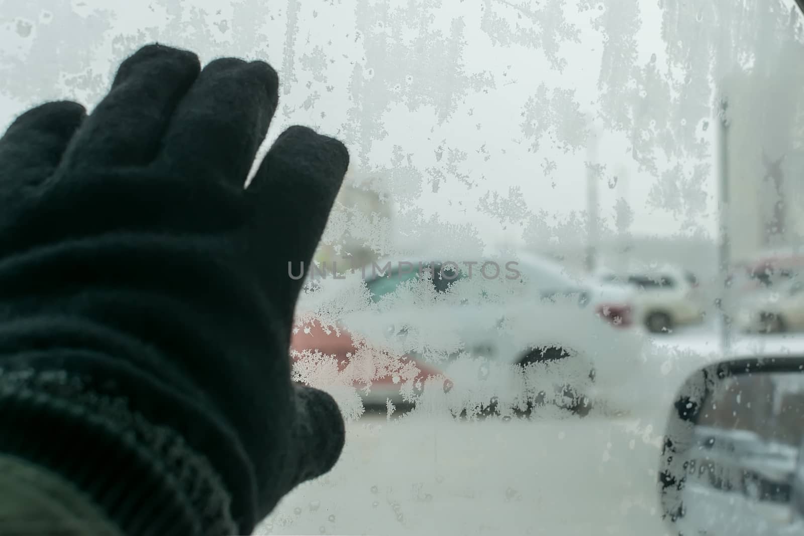 the hand of a man in a winter glove touches the icy glass of the car by jk3030