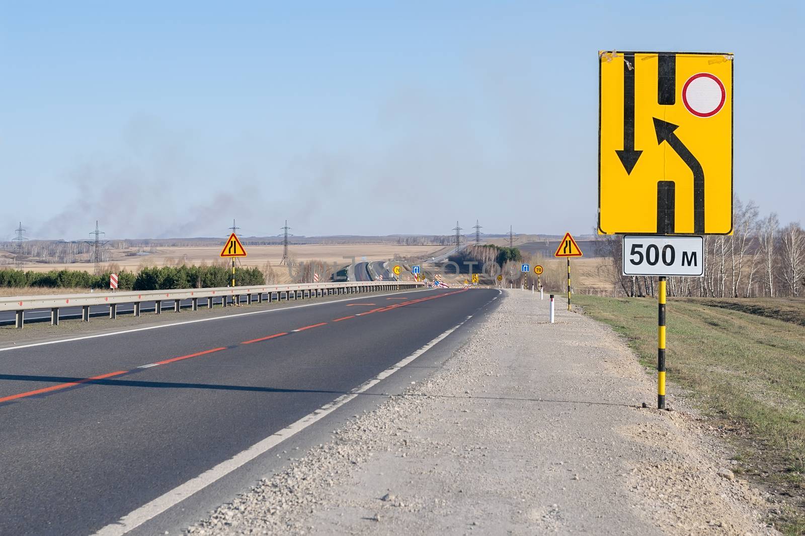 view of a large number of road repair warning signs on a country highway on a new asphalt surface in a hilly area