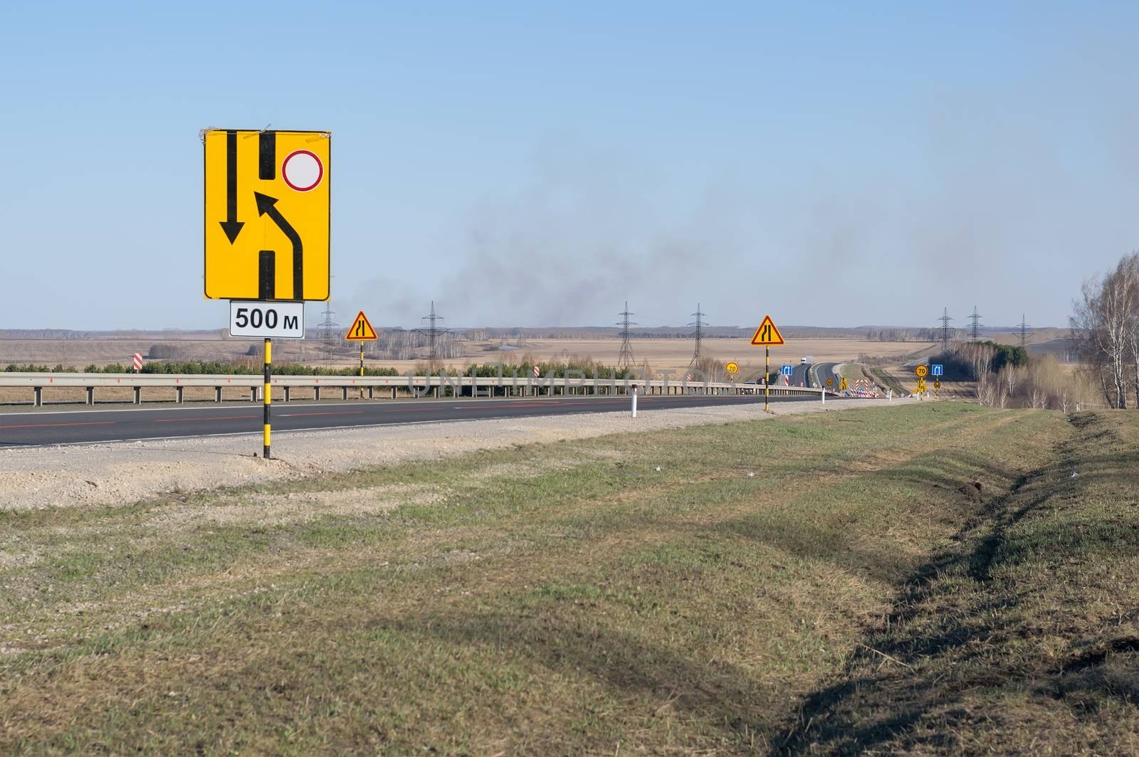 view of a large number of road repair warning signs on a country highway on a new asphalt surface in a hilly area