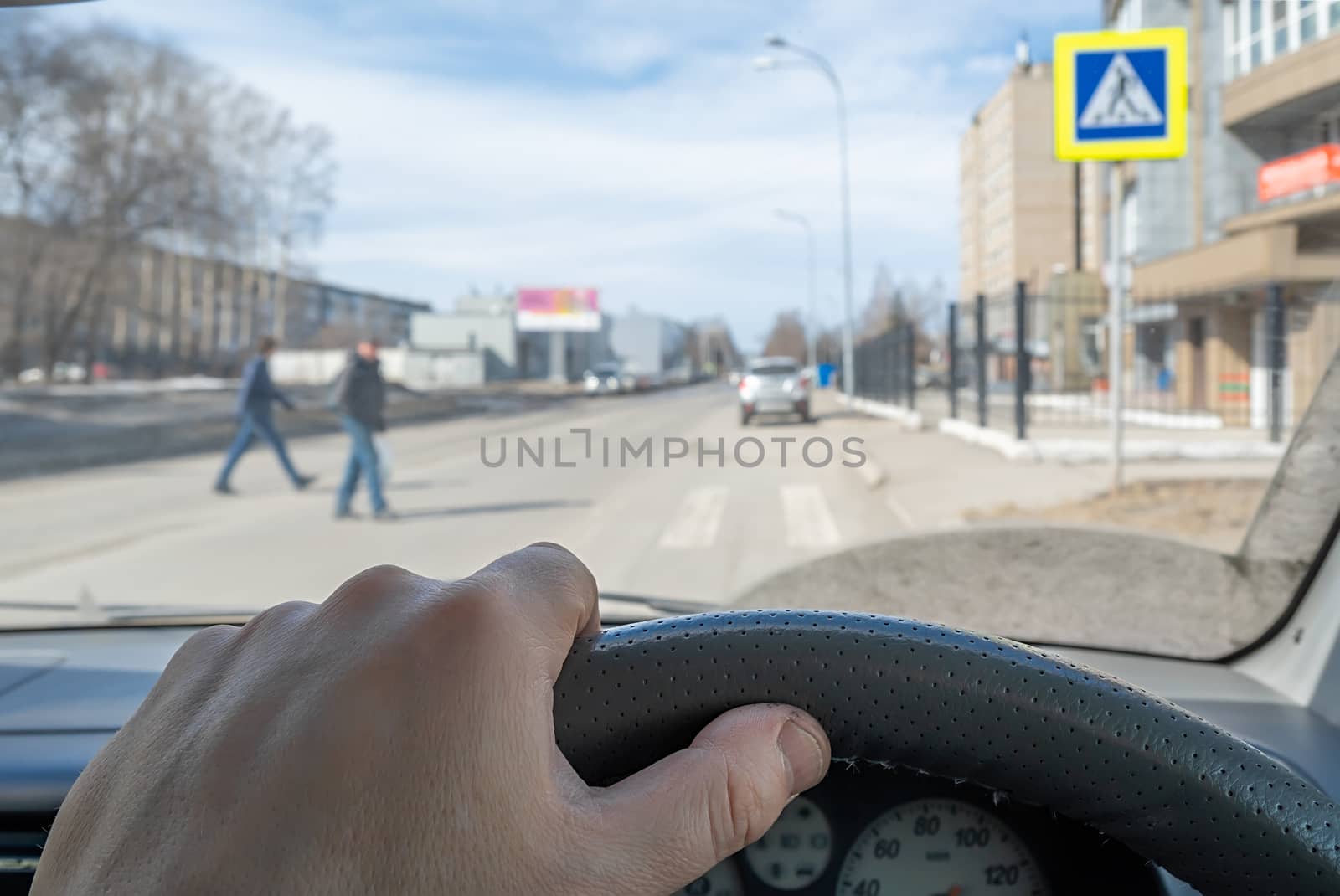 view from the car, the driver hand on the steering wheel of the car, located opposite the pedestrian crossing and pedestrians crossing the road