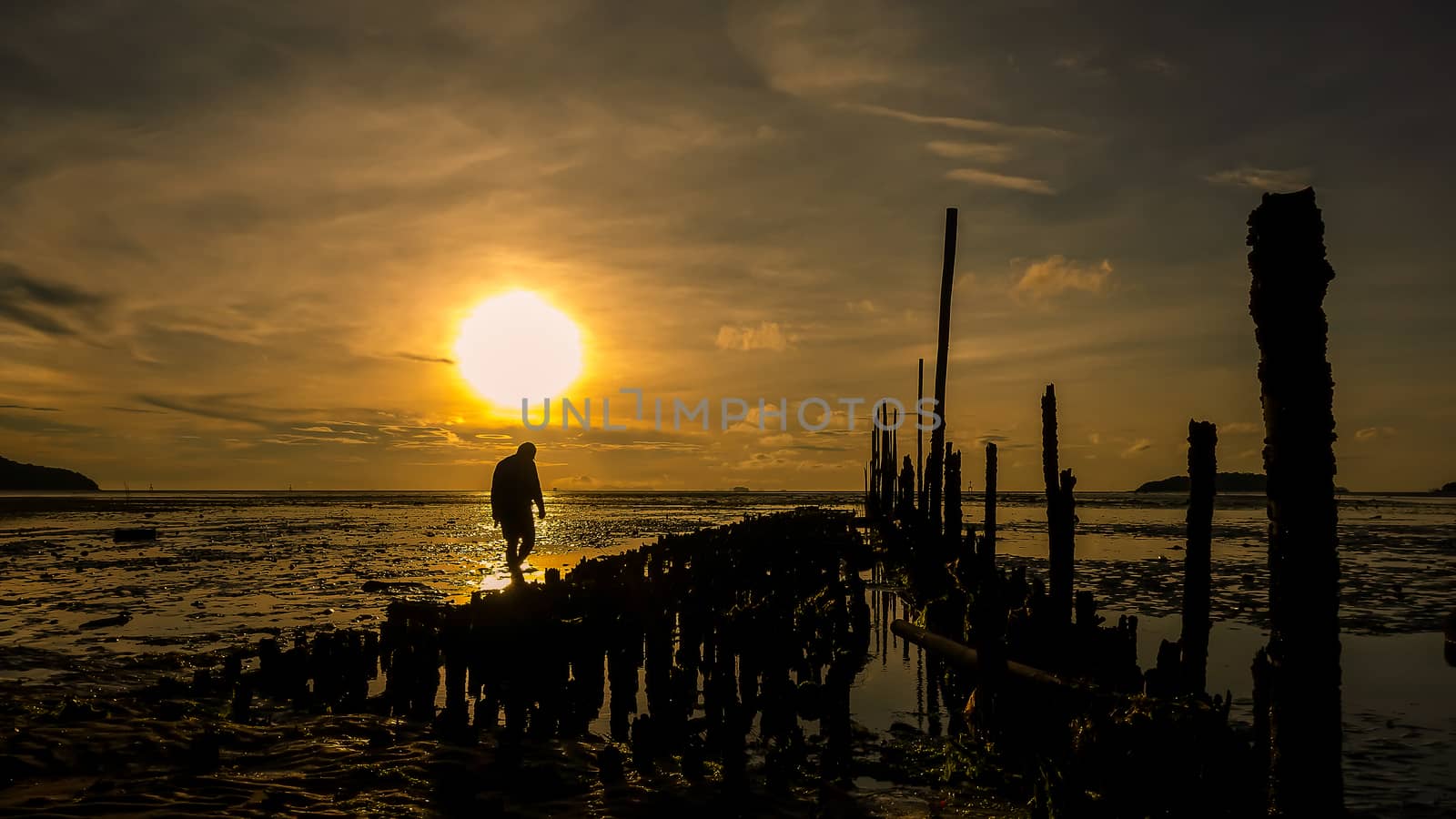 Silhouette of man walking on the beach at sunrise  by YingTanthawarak