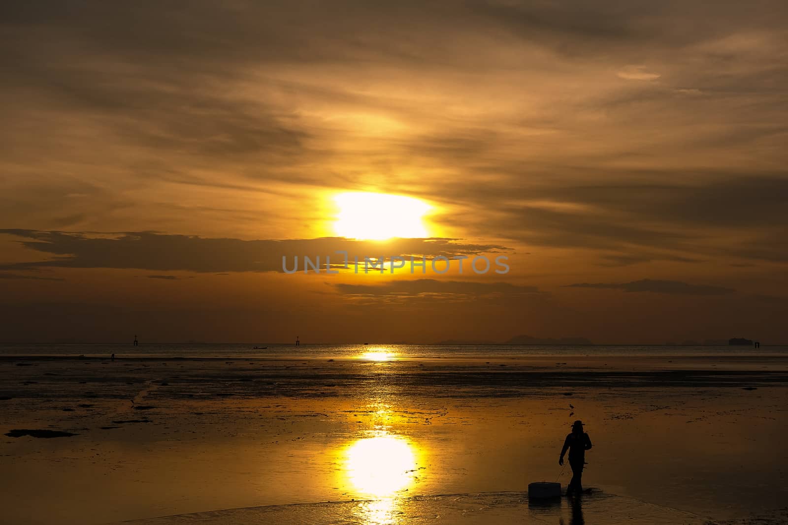 Silhouette of man walking on the beach at sunrise , beautiful cloudy sky reflected on the beach.
