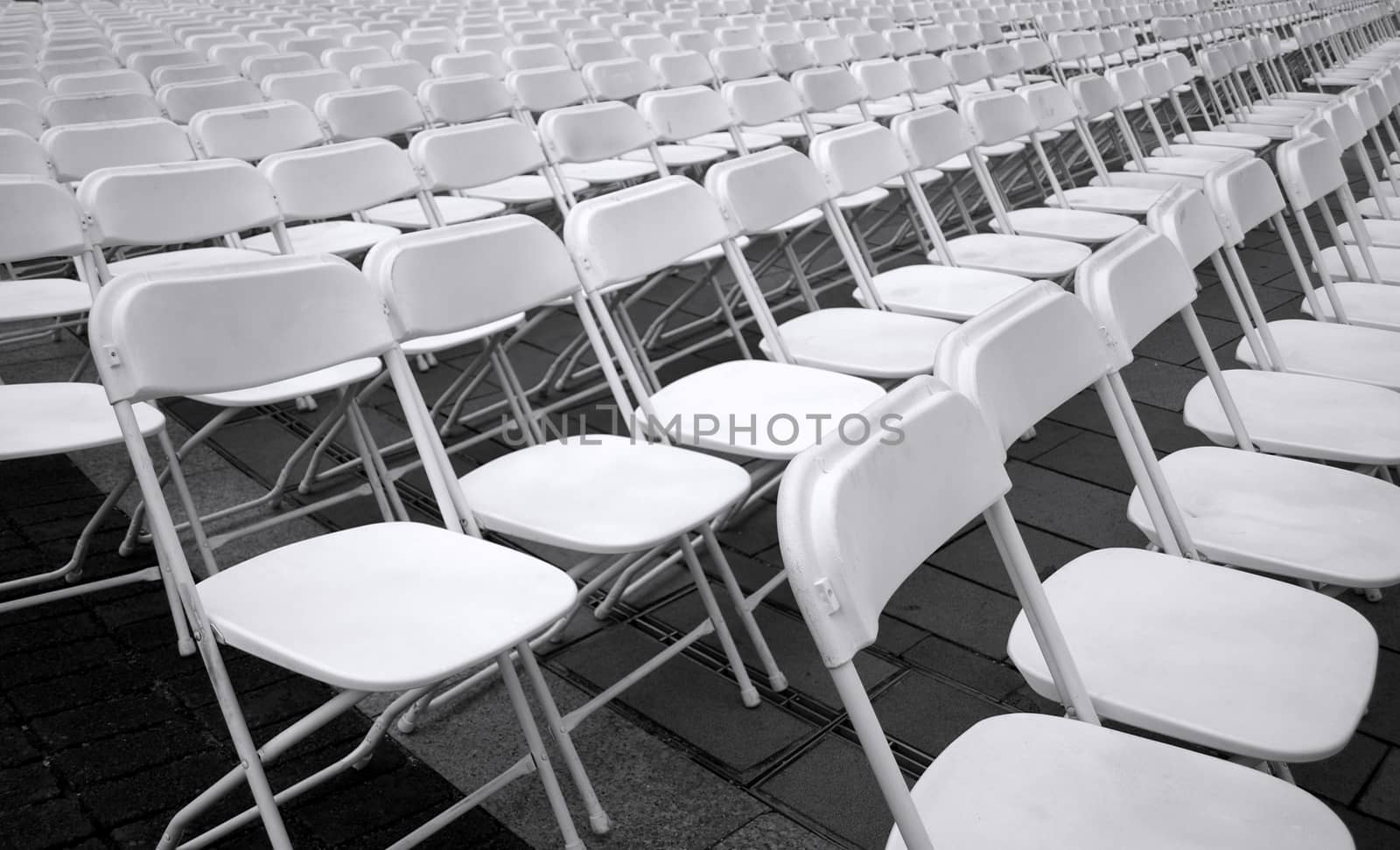 Plastic folding chairs are set up for an outdoor concert
