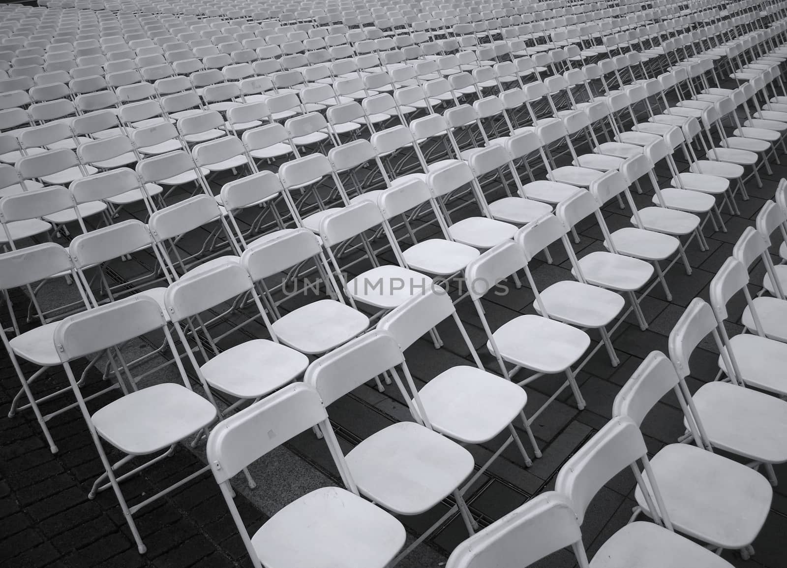 Row after row of plastic chairs are set up for an outdoor concert
