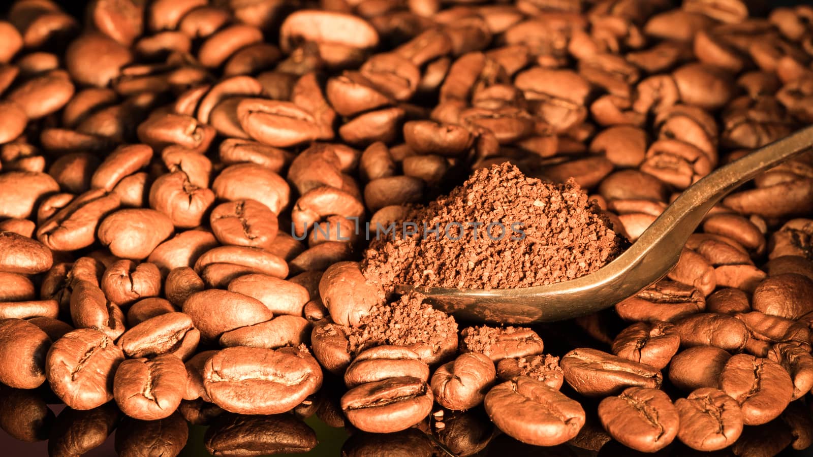 Coffee beans close-up with a spoon of ground coffee on a mirror background.