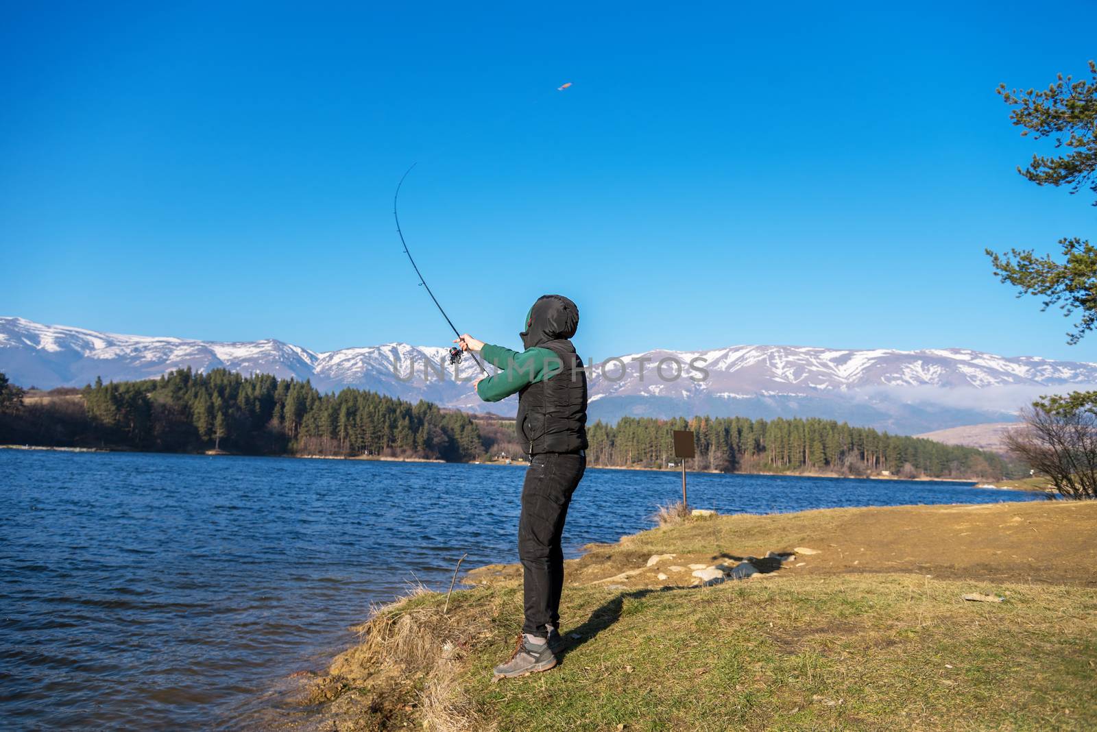 A male fisherman on the lake is standing in the water and fishing for a fishing rod. Fishing hobby vacation concept. Copy space.