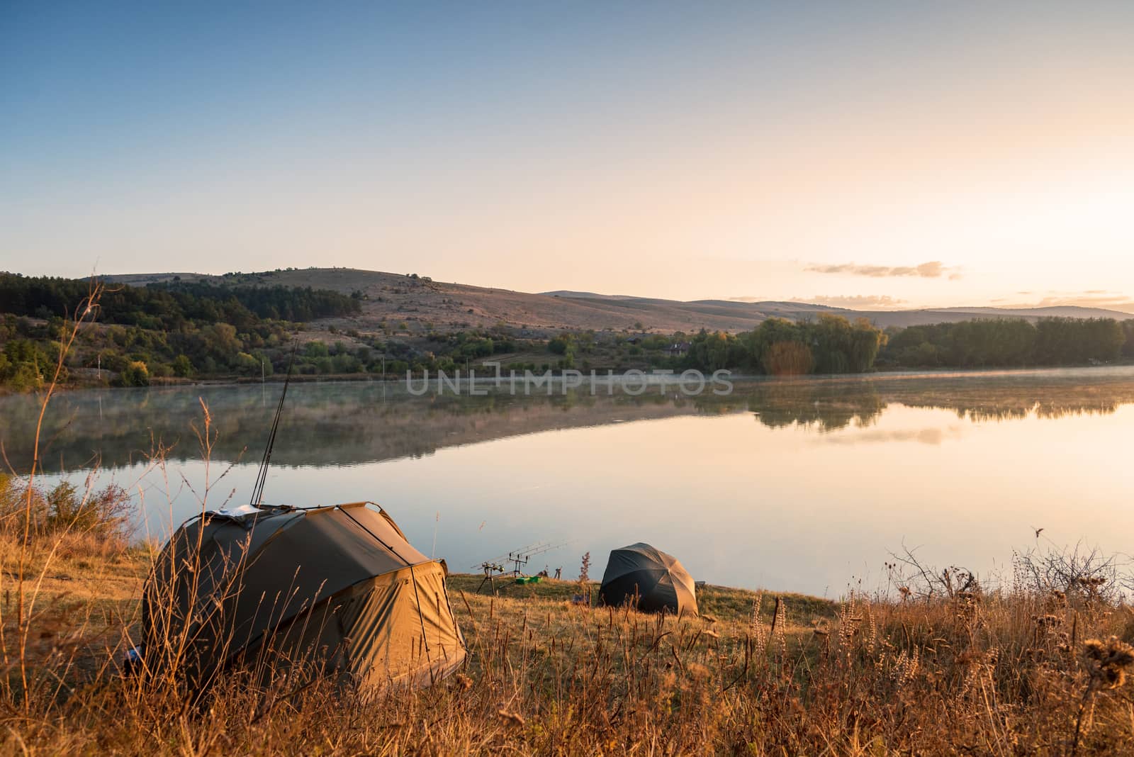 Fishing adventures, carp fishing. Angler, at sunset, is fishing with carp fishing technique. Camping on the shore of the lake.