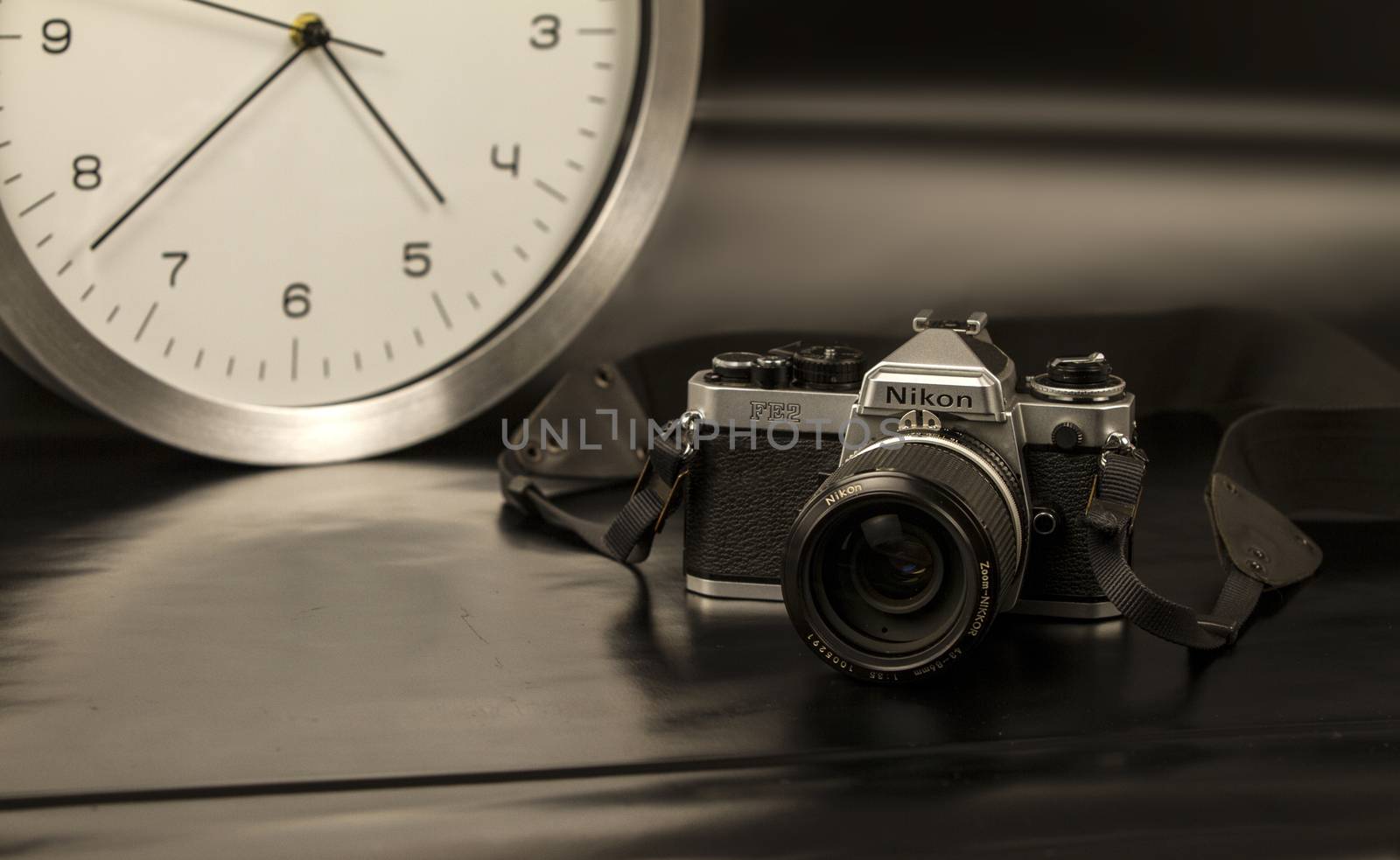 The frenzy of today's times in contrast with the past. A modern design wall clock next to a vintage camera on a black background with a sepia effect