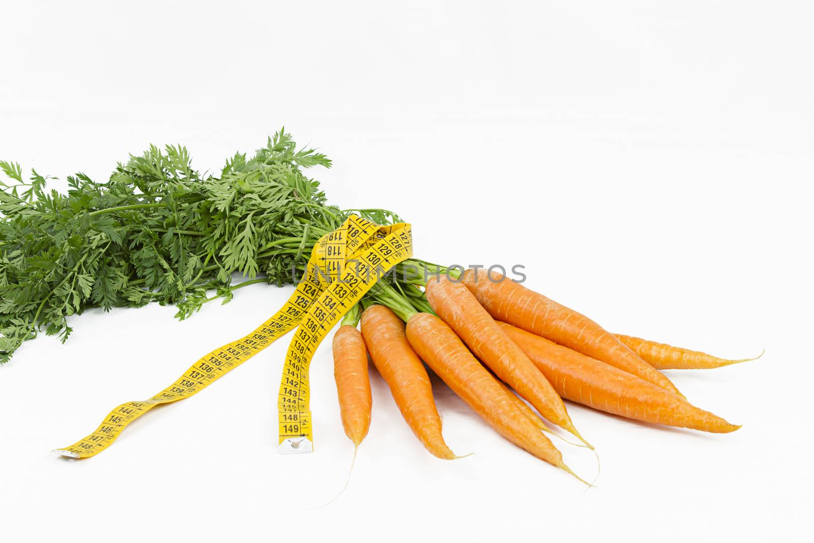 Vegetarian diet to reduce weight. A bunch of freshly picked carrots wrapped in a body measuring tape ruler which symbolizes the waistline