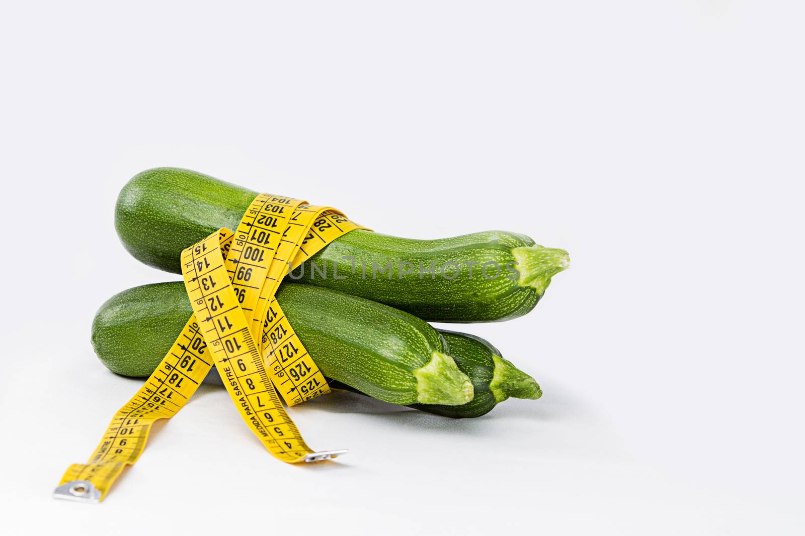 Vegetarian diet to reduce weight. Three freshly picked courgettes wrapped in a body measuring tape ruler that symbolizes the waistline